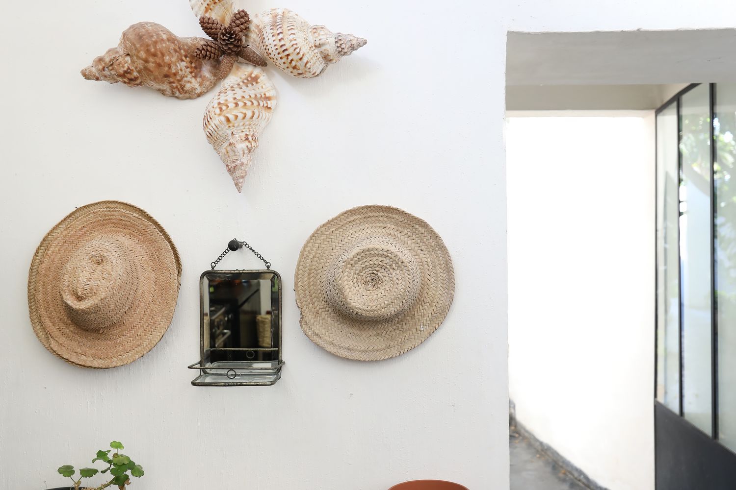 Un détail de la maison — coquillages, chapeaux de paille et vaisselle blanche sur la console